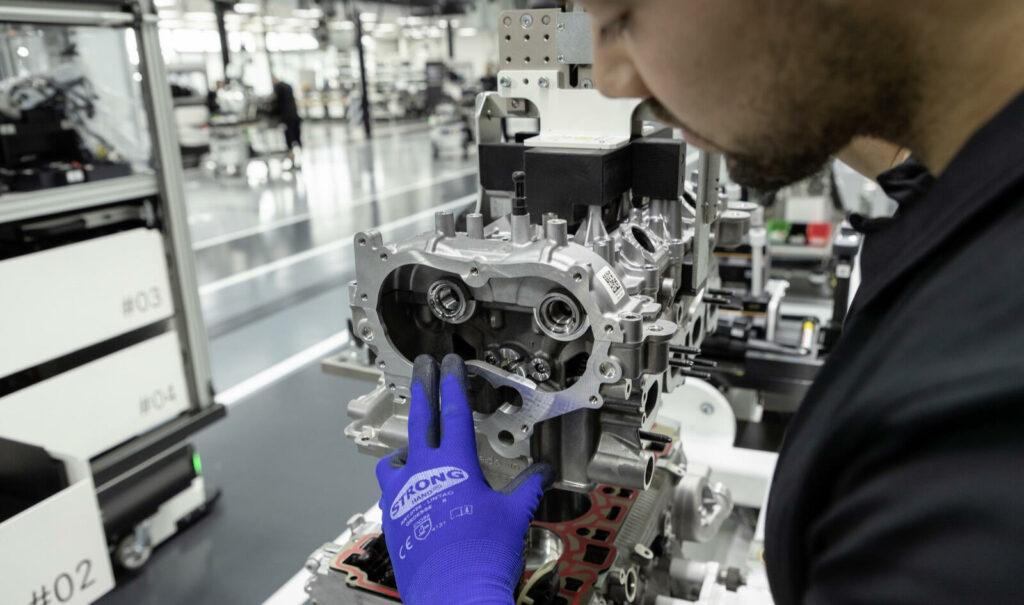 En man arbetar med en bilmotor i en fabrik. (AI text)