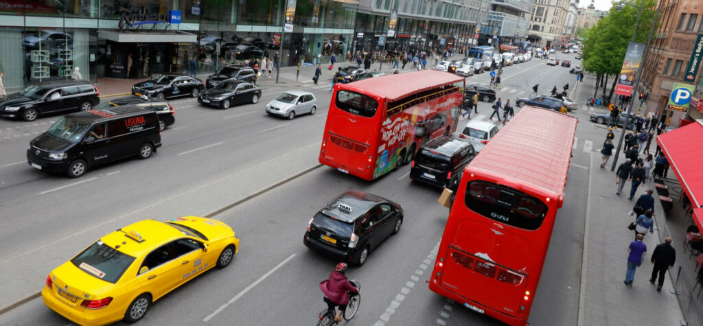 En stadsgata med många bilar och folk. (AI text)