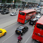 En stadsgata med många bilar och folk. (AI text)