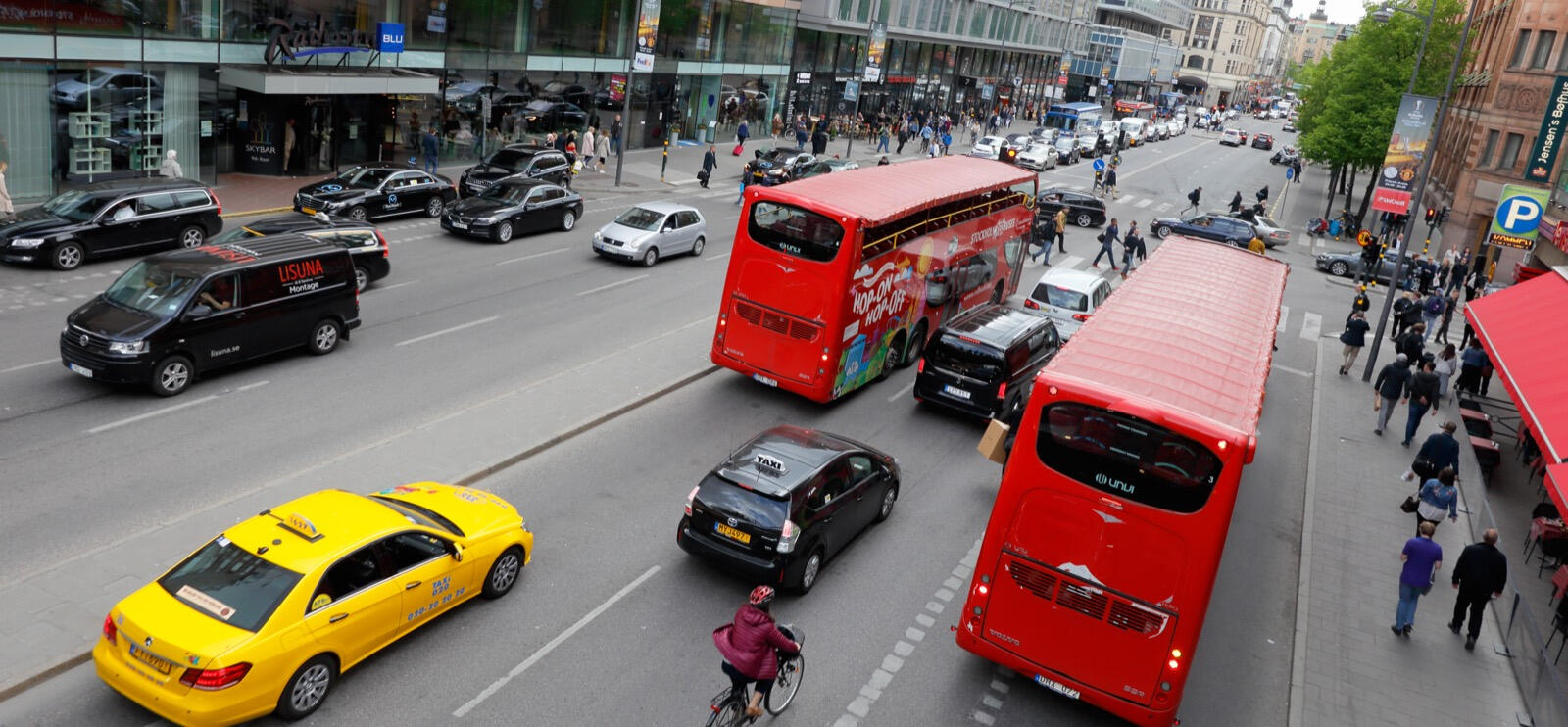 En stadsgata med många bilar och folk. (AI text)