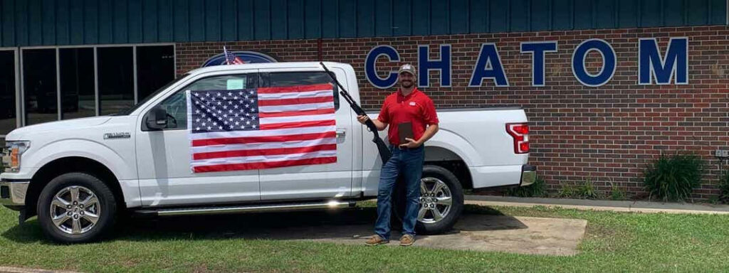 En man står utanför en Ford-återförsäljare med en amerikansk flagga. (AI text)