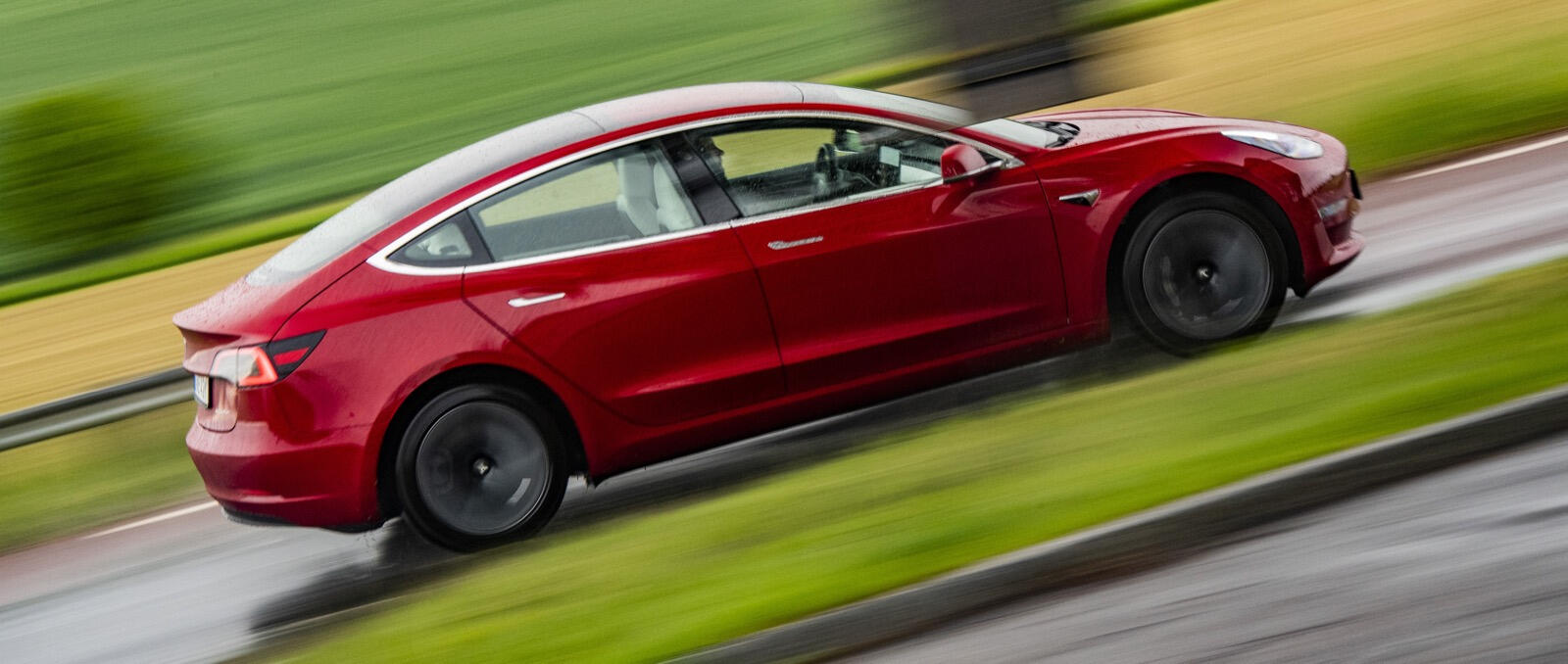 Tesla Model 3 körs på en blöt väg. (AI text)