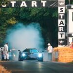 En bil kör nedför en väg med höskurar i bakgrunden. (AI text)