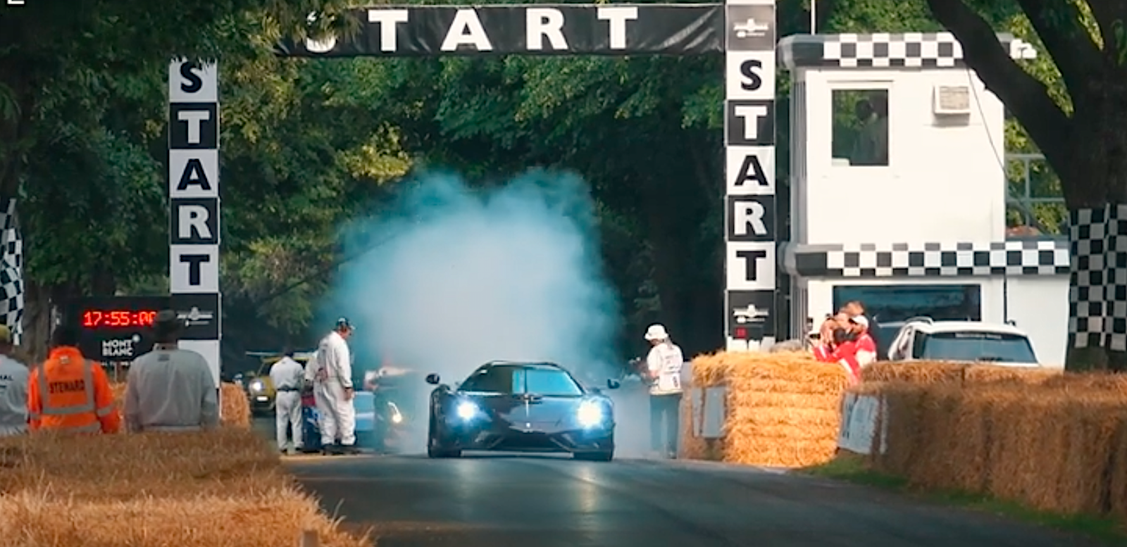 En bil kör nedför en väg med höskurar i bakgrunden. (AI text)