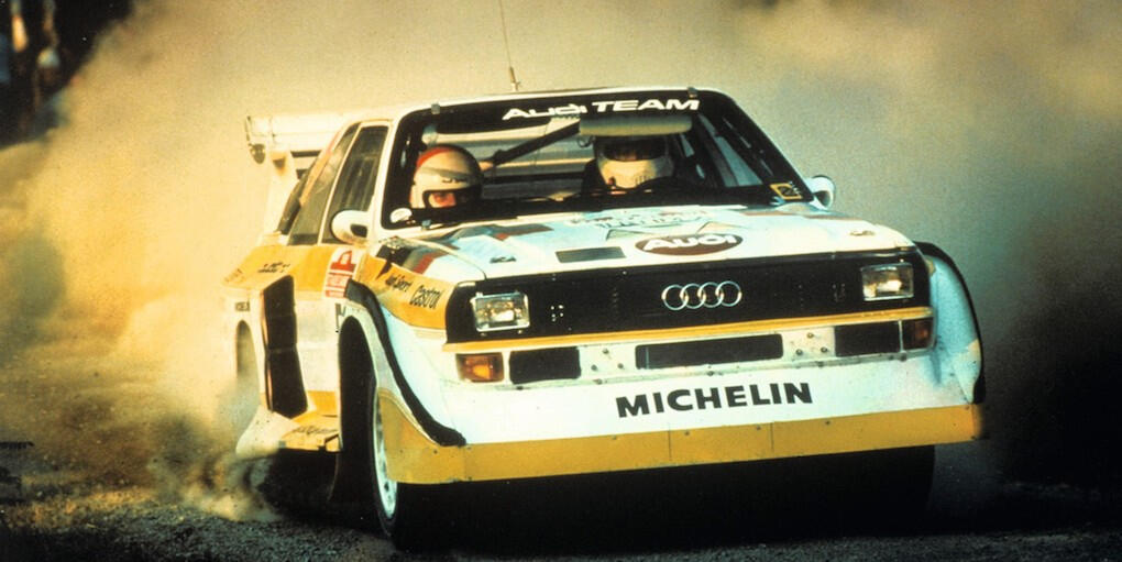 En Audi rallybil kör genom en skog. (AI text)