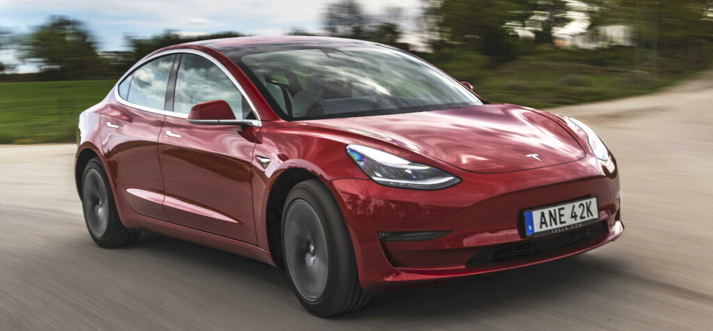 En Tesla Model 3 kör längs en landsväg. (AI text)