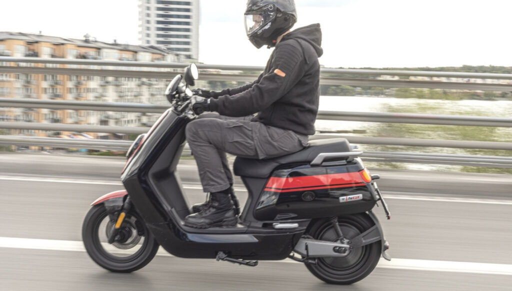 En person cyklar med en scoot på en stadsgata. (AI text)