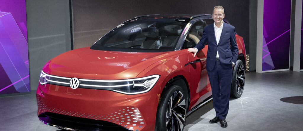 En man i kostym står bredvid en röd Volkswagen ID.4. (AI text)