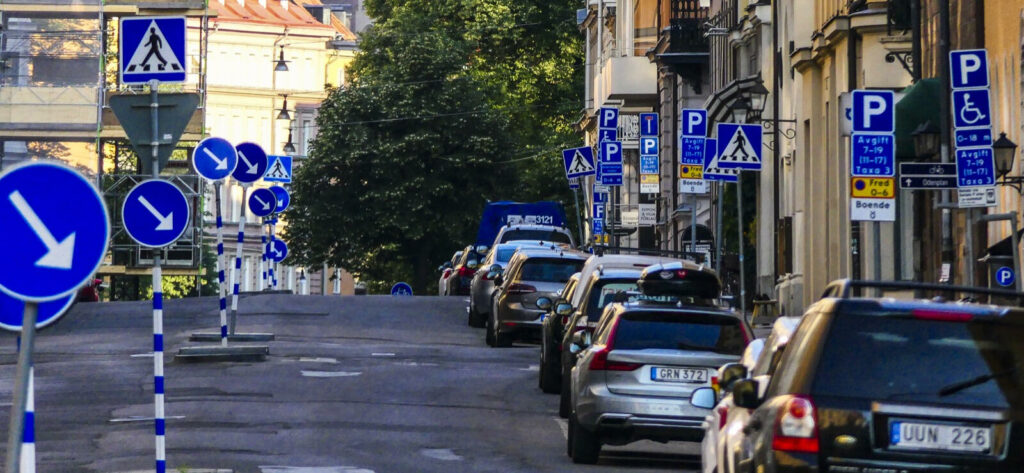 En smal gata med parkerade bilar. (AI text)