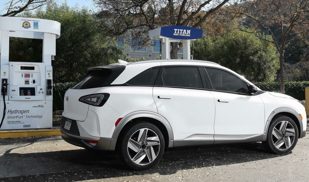 En vit elbil parkerad vid en bensinstation. (AI text)