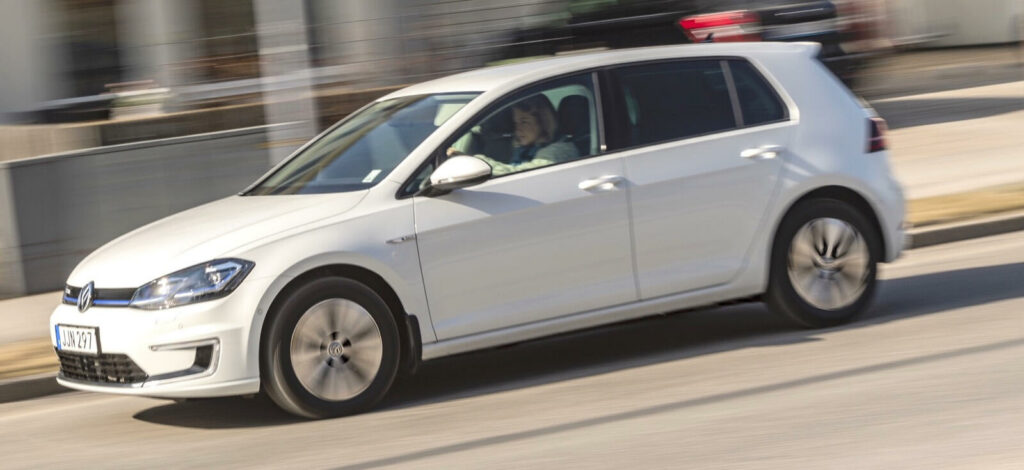 En Volkswagen Golf E EV kör nedför en stadsgata. (AI text)