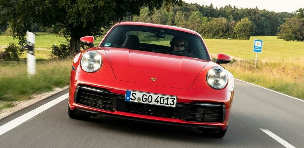 En röd Porsche 911 GTS kör nerför en landsväg. (AI text)