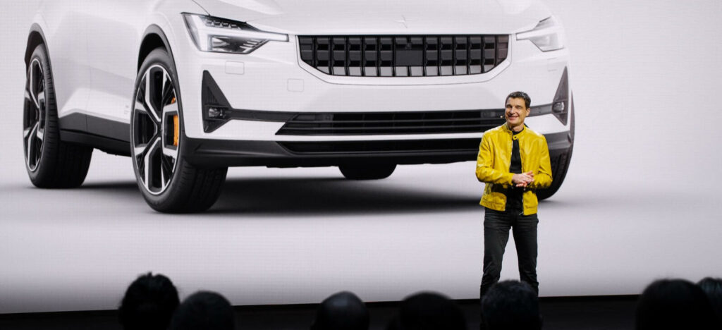 En man står på en scen framför en vit SUV. (AI text)