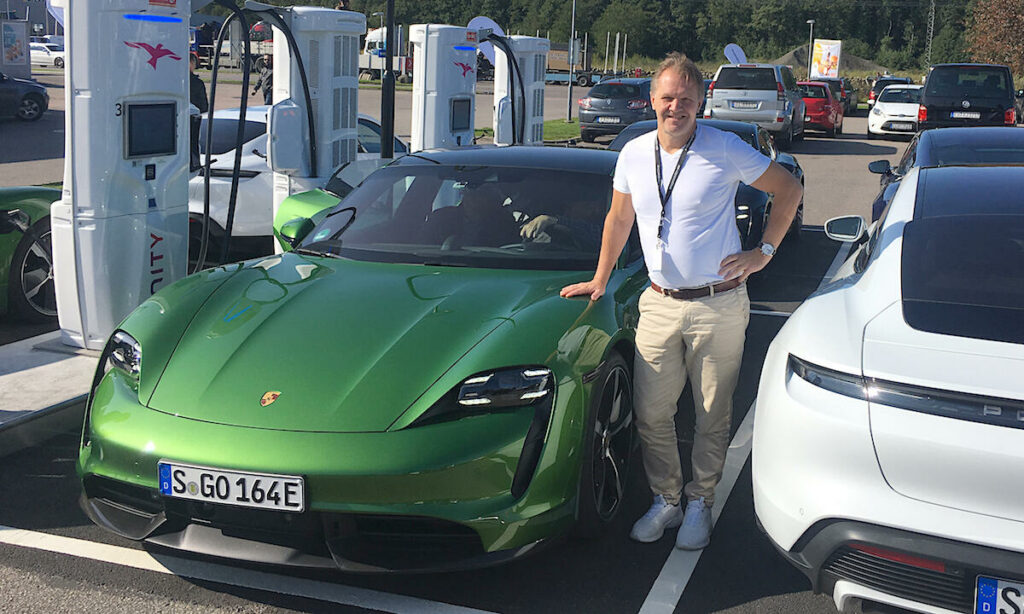 En man står bredvid en grön Porsche EV. (AI text)