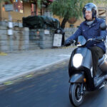 En person cyklar på en scootar längs en stadsgata. (AI text)