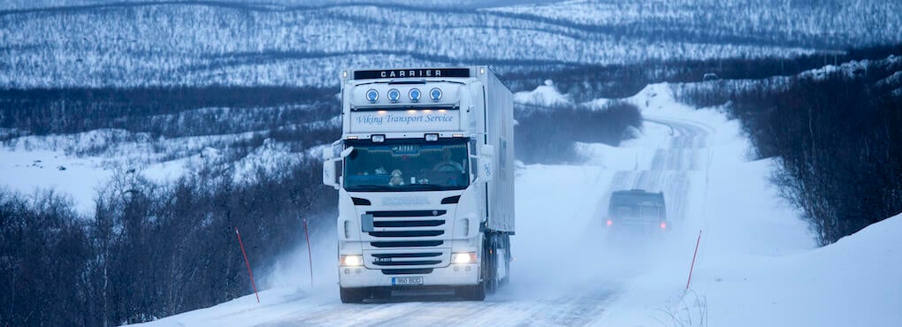 En lastbil kör nedför en snöig väg. (AI text)