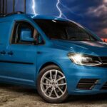 En blå Volkswagen-buss parkerad framför ett byggnad med lågor. (AI text)