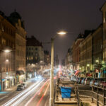 En stadsgata på natten med bilar som kör längs den. (AI text)