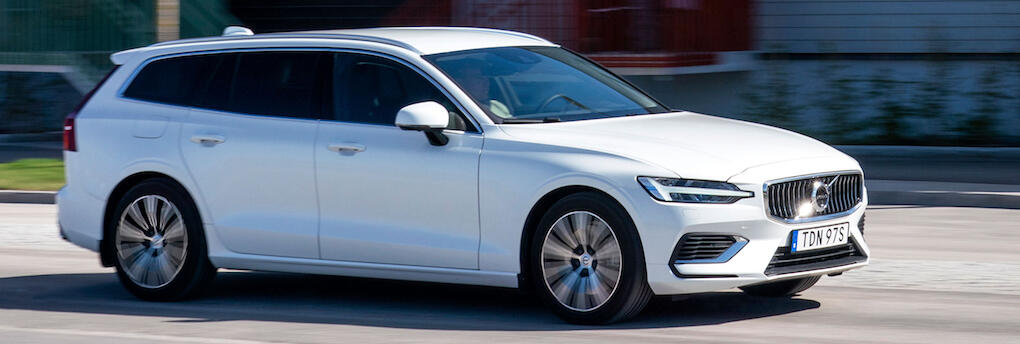 En vit Volvo V90 SUV kör nerför en gata. (AI text)