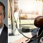 En man i kostym och slips står bredvid en bil som laddas på en elbilstation. (AI text)