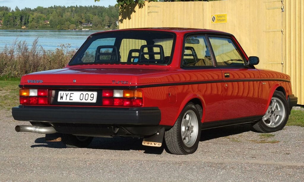 En röd bil parkerad framför ett byggnad. (AI text)