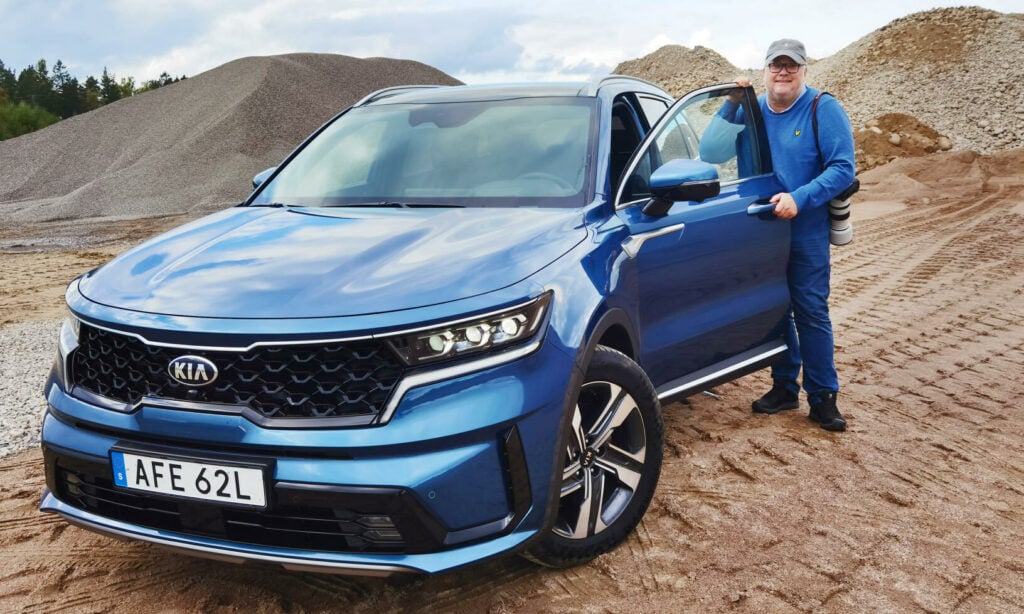 En man står bredvid en blå Kia SUV. (AI text)