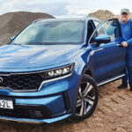 En man står bredvid en blå Kia SUV. (AI text)