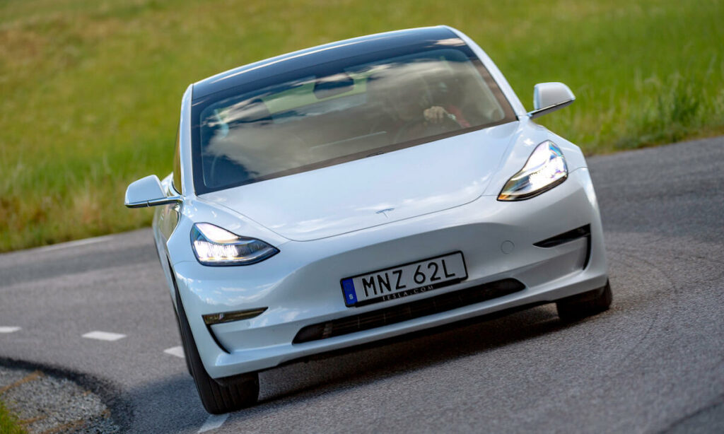 En Tesla Model 3 kör nerför en landsväg. (AI text)