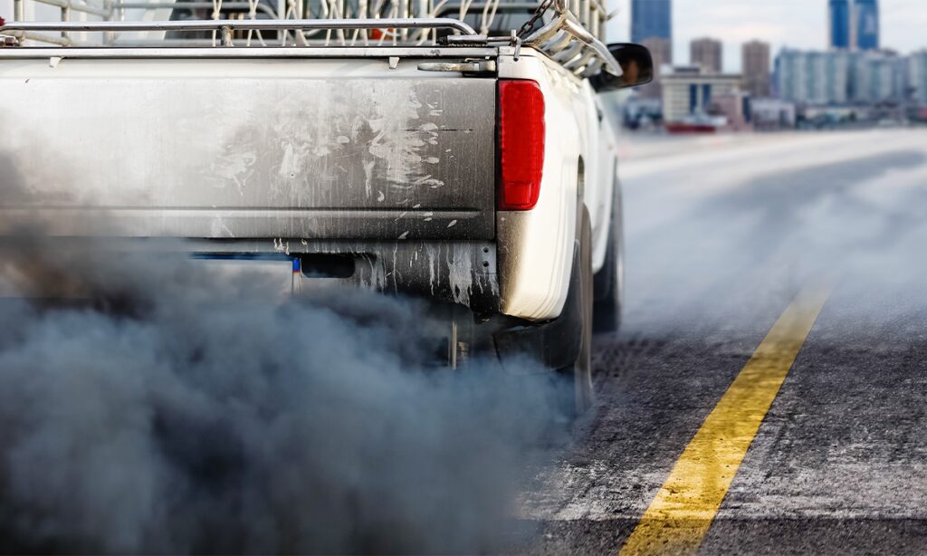 En lastbil kör längs vägen med rök som kommer ut ifrån den. (AI text)