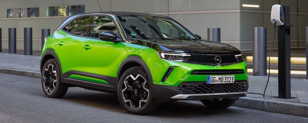 En grön Opel Cruise parkerad framför en laddstation. (AI text)