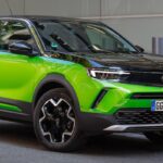 En grön Opel Cruise parkerad framför en laddstation. (AI text)