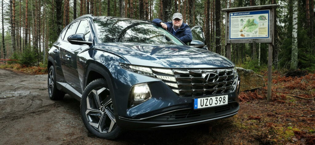 En man står bredvid en SUV i skogen. (AI text)