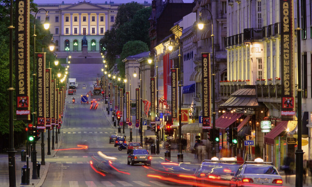 En stadsgata på natten med bilar som kör längs den. (AI text)