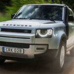 En Land Rover Defender kör längs en grusväg. (AI text)