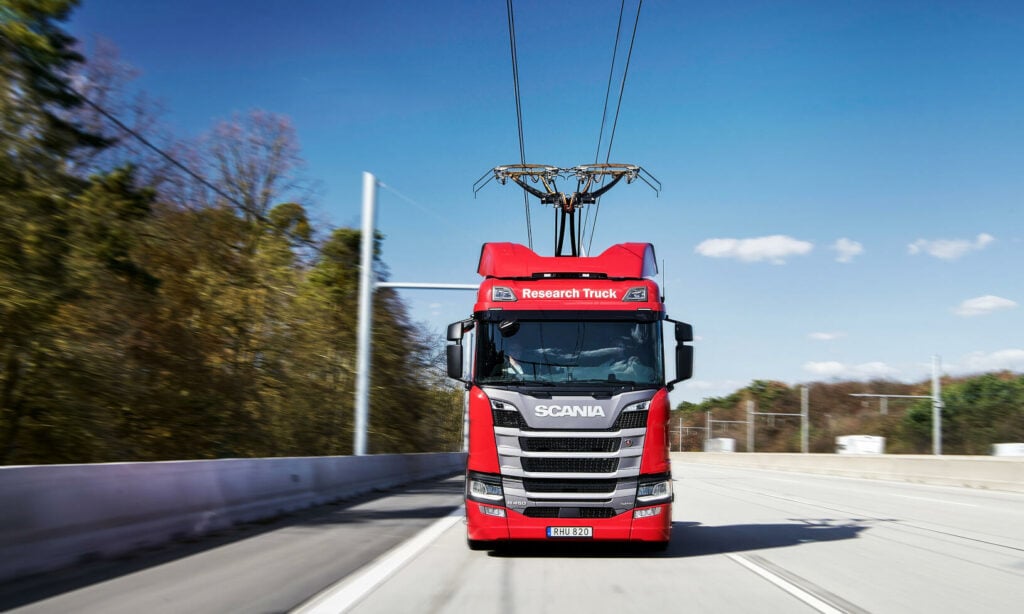 En röd lastbil kör nedför en motorväg. (AI text)