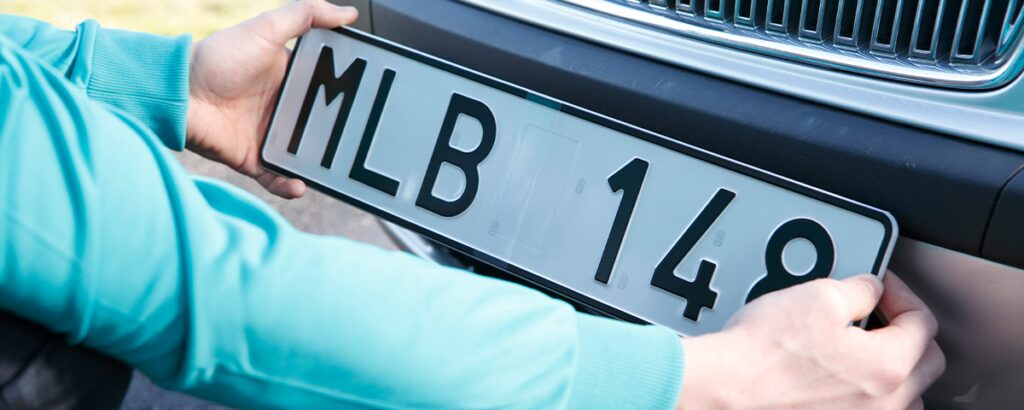 En man monterar en bilplåt på sin bil. (AI text)