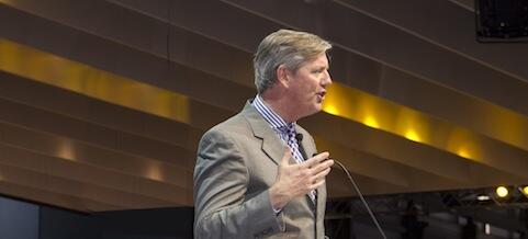 En man håller ett tal på en konferens. (AI text)