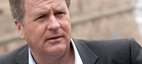 En man i kostym och slips tittar på kameran. (AI text)