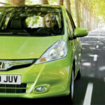 En grön Honda Jazz kör ner en väg. (AI text)