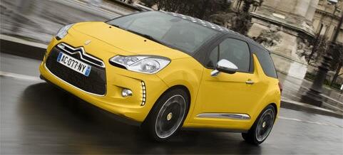 En gul Citroën C3 kör nedför en stadsgata bredvid en DS3. (AI text)