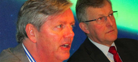 En man i kostym och slips pratar med en annan man i kostym och slips. (AI text)