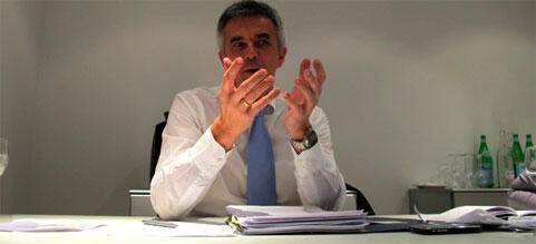 En man sitter vid ett bord och pratar med en kamera. (AI text)