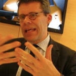 En man i kostym och slips pratar inför en kamera. (AI text)