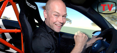 En man leder i en racingbil och ler. (AI text)