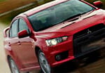 En röd Mitsubishi Lancer GT med bakväxel kör på en grusväg. (AI text)