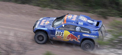 En blå rallybil kör nerför en grusväg. (AI text)