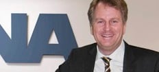 En man i kostym och slips står framför en NA-logga. (AI text)