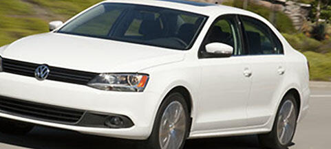 En vit Volkswagen Jetta kör nerför en väg. (AI text)