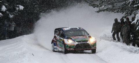 En rallybil körer nedför en snöig väg. (AI text)