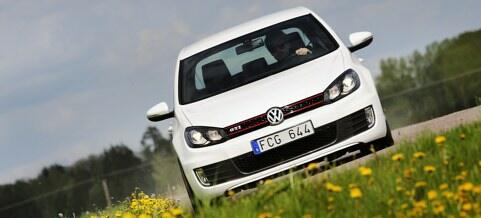 En vit Volkswagen Golf GTI kör nerför en väg. (AI text)